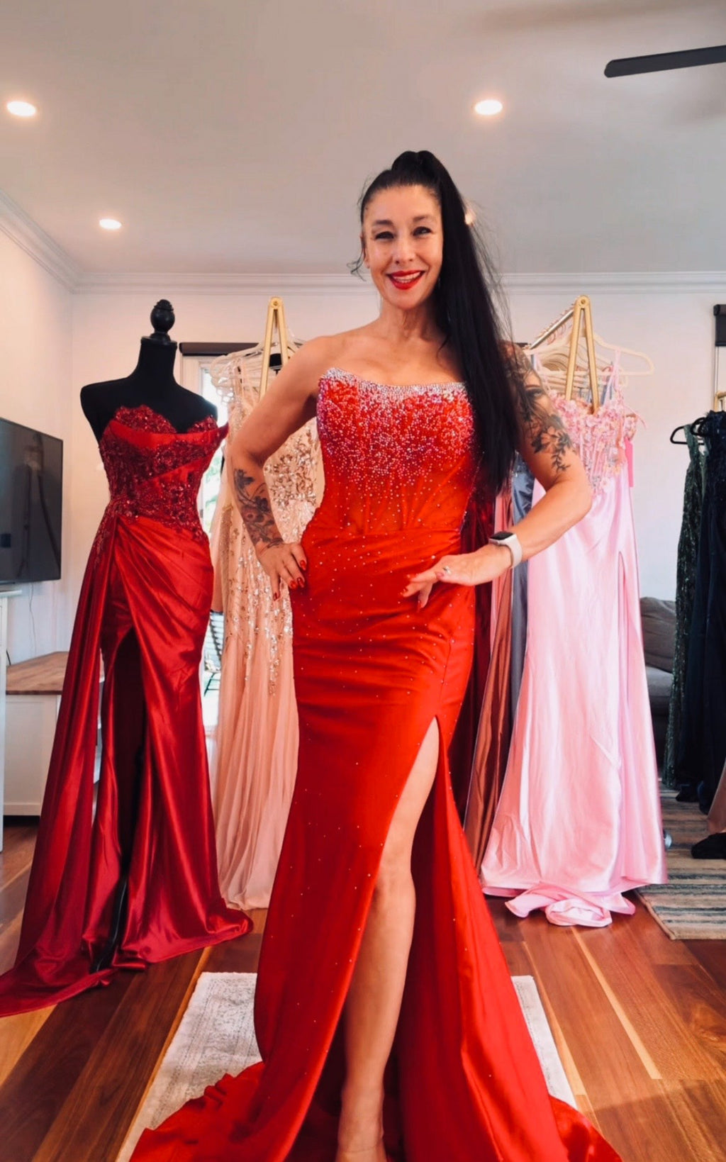 Woman in a red evening gown standing in a room with mannequins wearing dresses.